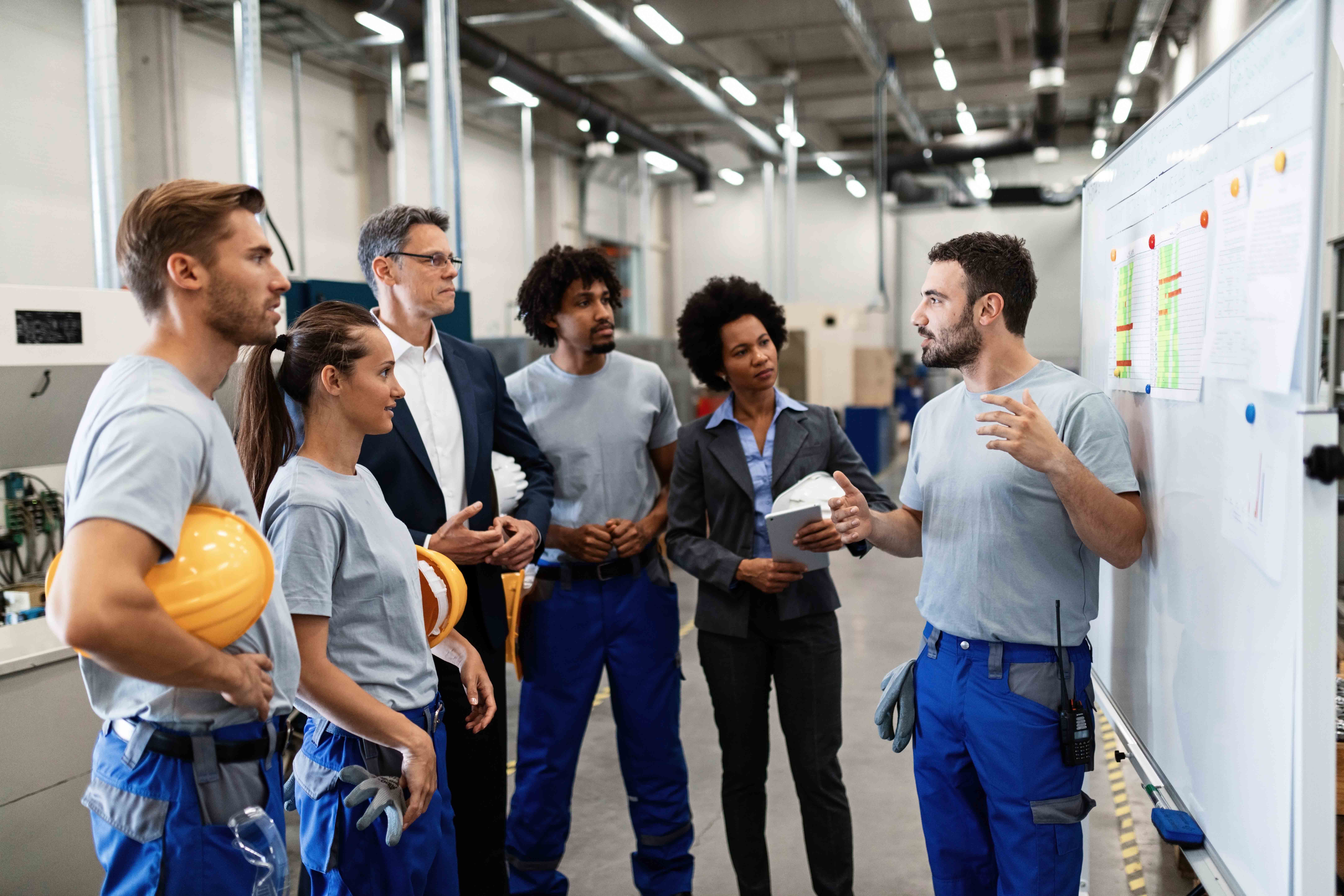 Manual worker communicating with company leaders and his coworkers during business presentation in a factory.